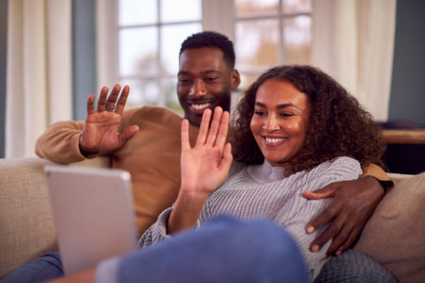 istock Smiling Couple Sitting On Sofa At Home Making Video Call On Digital Tablet 1389708573