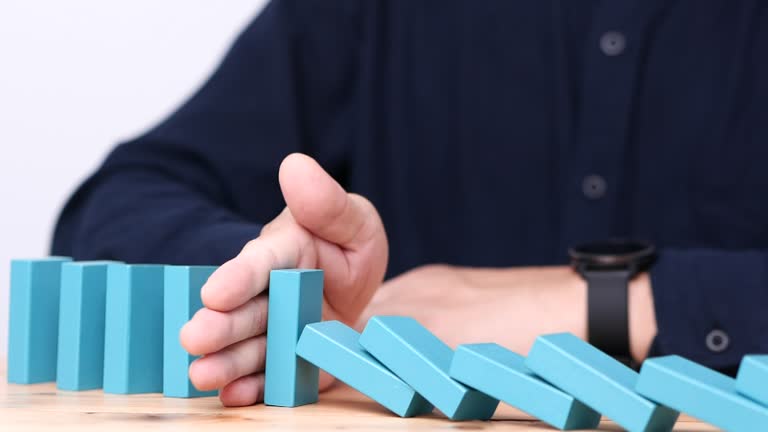 Businessman hand stopping continuous failing domino wooden effect. Concept of Risk Management, Business Crisis, Domino Effect, Investment, Finance, Risk, Disaster, Protection, Prevention, Opportunity