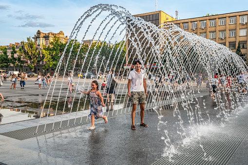 Mykolaiv, Ukraine - July 25, 2020: Happy people inside the arched fountain on the city square in Mykolaiv. Adults and children have fun among the cool jets of water on a hot summer evening