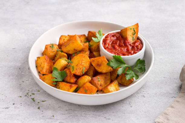 traditionelle spanische kartoffel, patatas bravas mit geräuchertem paprika, würzige tomatensauce und petersilie in einer weißen schüssel auf grauem steinhintergrund, draufsicht. leckeres hausgemachtes essen - patatas bravas stock-fotos und bilder