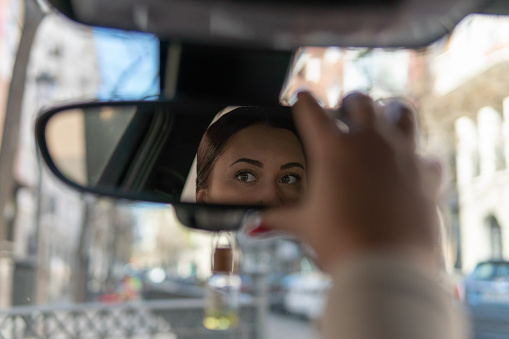 Young woman holding the sun protection flap of the car with the intention of looking through the mirror before getting out or starting to drive.