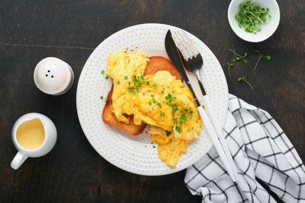 istock Scrambled Eggs. Fluffy and Buttery scrambled eggs on bread with microgreen radish and hollandaise sauce on white plate over dark old wooden background. Homemade breakfast or brunch meal. Top view. 1389719404