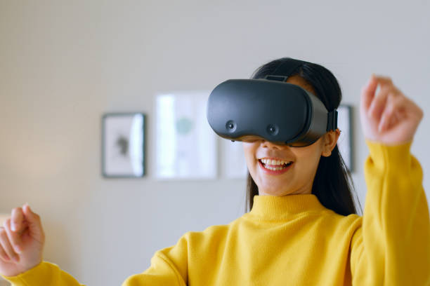 istock Young Asian woman dancing while using 360 VR headset for virtual reality/ metaverse at home 1389719466