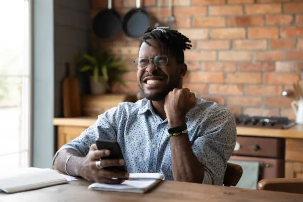 Photo of Overjoyed millennial African guy reading message on smartphone