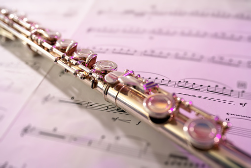 Flute Detail with Sheet Music - Musical instrument detail with selective focus on area of flute and sheet music notes in background. Pink accent light for colorful highlights.
