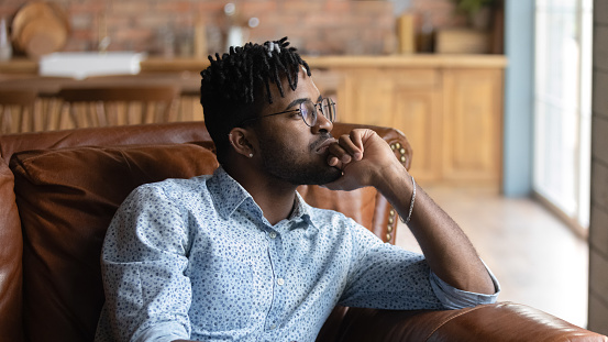 Thoughtful bored millennial Black mixed race guy lost in thoughts