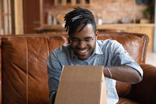 istock Happy millennial Afro American hipster guy unpacking parcel at home 1389719822