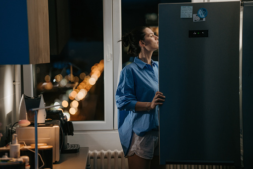 Woman opening the fridge and looking inside, at night in her kitchen at home