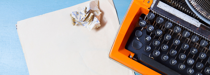 Workspace with orange vintage typewriter and empty paper on blue background, flat lay scene