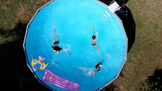 Above Aerial drone view on kids swimming in the rounded blue pool in the backyard