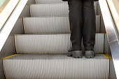 istock Legs in black pants on step of escalator in shopping mall. Metal staircase. Up escalator. Close-up. 1389724948