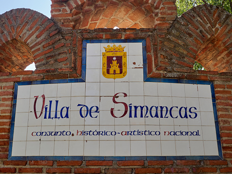 Brick and tiles sign in the entrance of Simancas, with the coat of arms, the name of the village and a sentence that says \