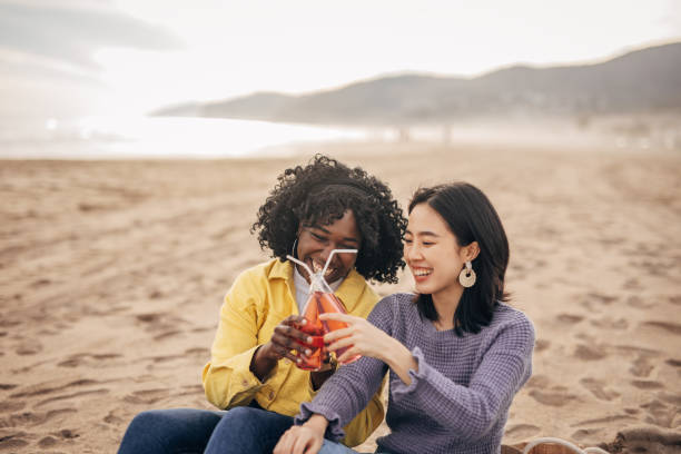 istock Two friends sitting on the beach having fun and drinking on the spring day 1389733448