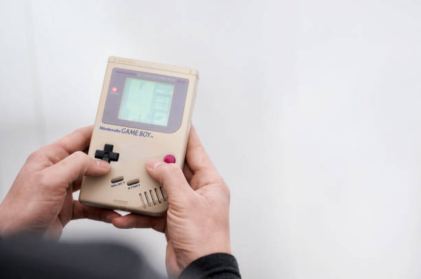 mann hält in seinen h�änden ein klassisches videospiel nintendo game boy, während er das beliebte spiel tetris spielt - nes stock-fotos und bilder