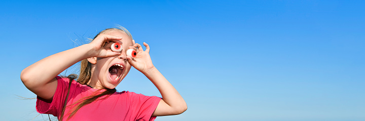 Surprised Teen girl in a pink t-shirt looks into the giant jelly eyes binoculars ahead. Banner with copy space