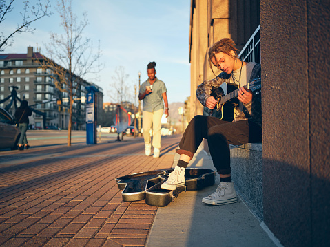 A young woman with tattoos and piercings playing guitar in the downtown area of a city.