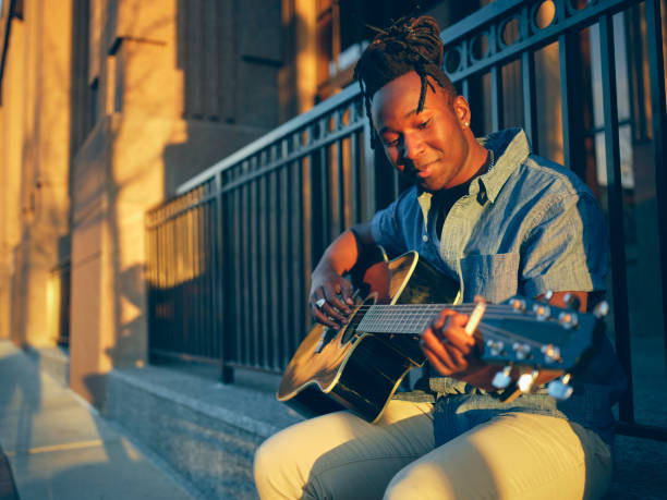 A young man playing guitar in the downtown area of a city.