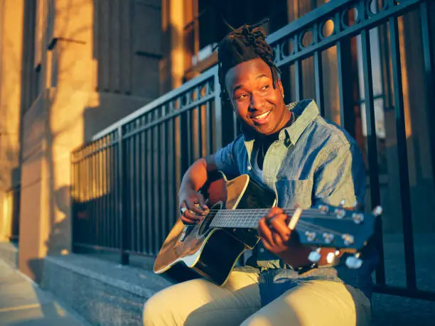 A young man playing guitar in the downtown area of a city.