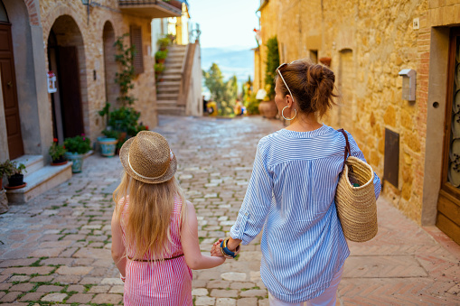 Travel in Italy. Seen from behind trendy mother and daughter in Tuscany, Italy sightseeing in Pienza.