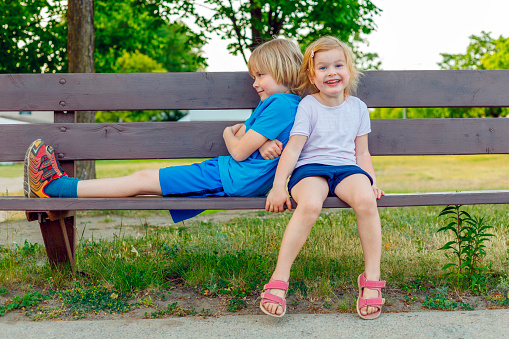 Children sitting on a bench in park in summer. Happy kids having fun. Smiling friends playing outdoors together