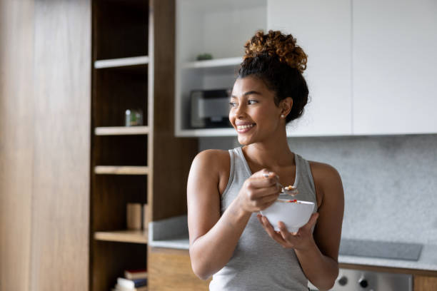 mujer feliz en casa comiendo un tazón de cereal para el desayuno - cereal breakfast granola healthy eating fotografías e imágenes de stock