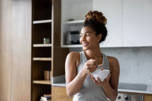 Happy African American woman at home eating a bowl of cereal for breakfast and smiling - healthy lifestyle concepts
