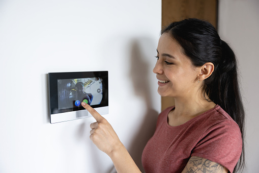 Latin American woman at home using the intercom to talk to a delivery person - lifestyle concepts. **DESIGN ON SCREEN WAS MADE FROM SCRATCH BY US**