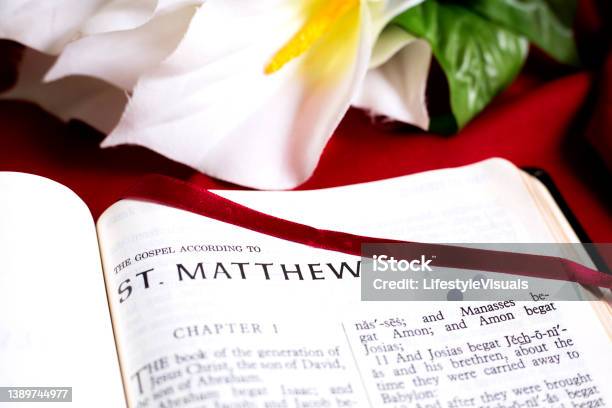 Bible Open To The Beginning Of The Book Of Matthew New Testament Red Satin Bookmark Is Across The Page Background Is A White Lily On Red Tablecloth Stock Photo - Download Image Now