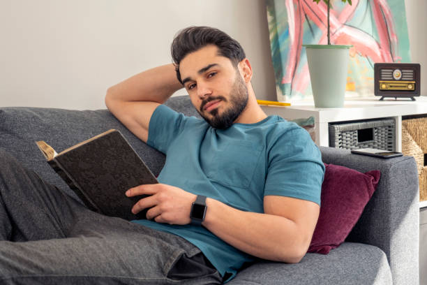 istock handsome young man reading a book at home 1389745223