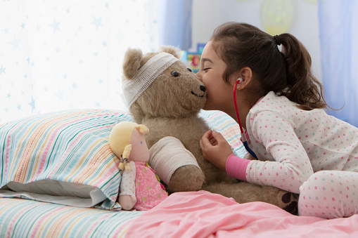 little girl playing doctor with teddy bear in bed