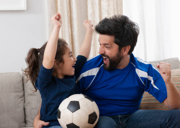 father watching sport game with daughter stock photo
