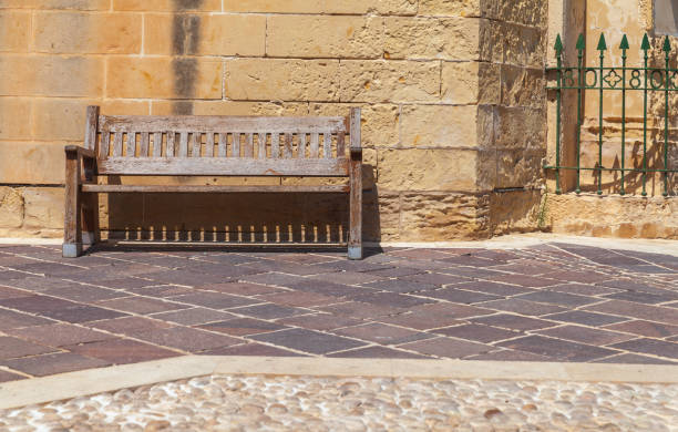 istock Empty wooden bench stands in front of stone wall 1389745842