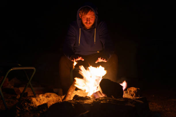 istock Blond man warming himself by the fire at dusk. Camping Concept 1389746415