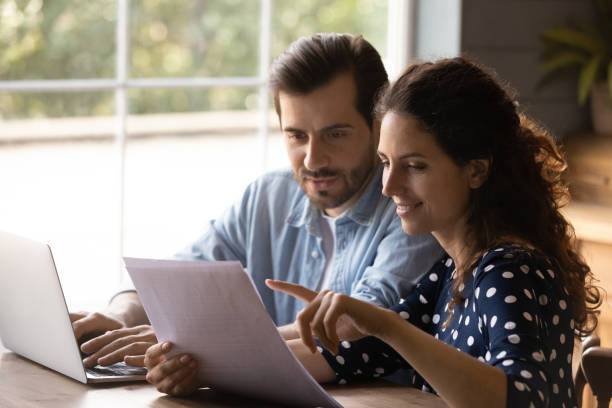 Young spouses hold bank account statement check financial data online Reading documents. Family couple study papers search information by loan mortgage affordable housing program on website. Young spouses clients hold bank account statement check financial data online benefits stock pictures, royalty-free photos & images