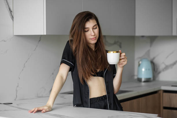 istock Young beautiful woman drinks morning coffee from white cup in kitchen. Rest and weekends. 1389746640
