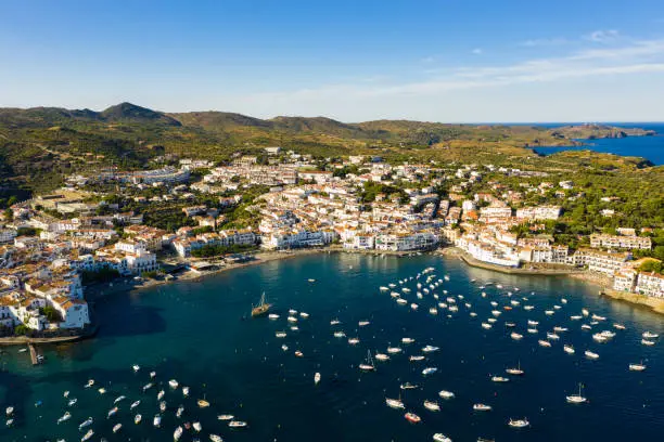 Scenic aerial view of Cadaques shoreline overlooking white buildings and boats parked in bay in summer, Catalonia, Spain