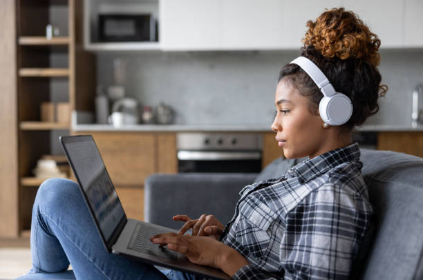 Woman at home working on her laptop and using headphones Young African American woman working on her laptop at home and using headphones Stream stock pictures, royalty-free photos & images