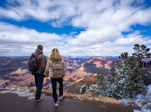 Man and woman  standing on top of the mountain enjoying beautiful winter landscape. People standing on the mountain cliff. Grand Canyon National Park, Arizona, USA.