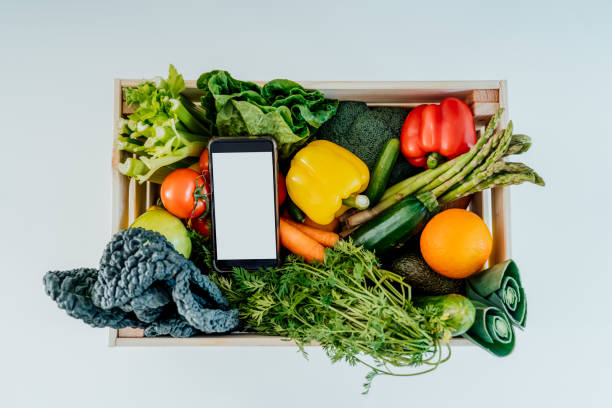 istock Top view wooden box with fresh vegetables and phone with blank white screen on white background. Mockup for online mobile application for diet program, food delivery, weight loss. Zero waste packing 1389751002