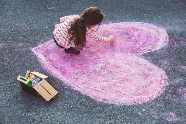 A five year old girl puts the finishing touches on a chalk heart drawing in her home's driveway.