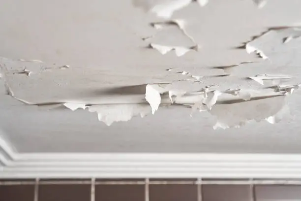 Photo of Damaged bathroom ceiling with cracked and peeling white paint on painted drywall close-up. Humidity and dampness in an apartment room