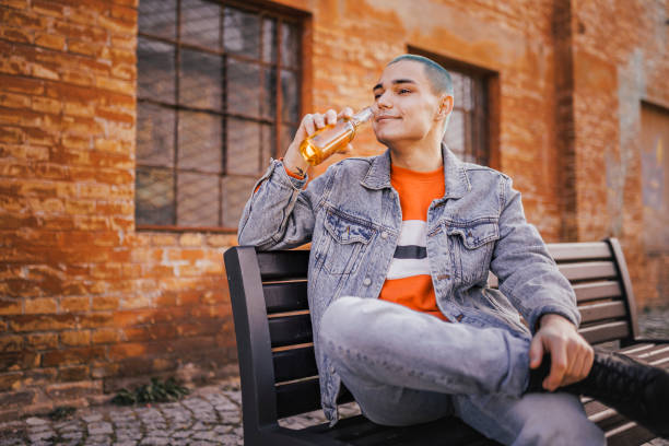 istock Hipster young man drinking beer on park bench 1389755727