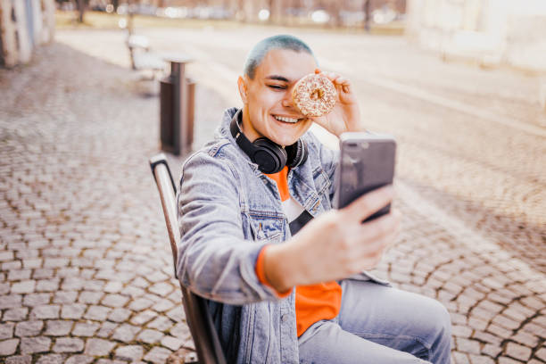 istock Man taking a funny selfie with donut by his smart phone 1389756078