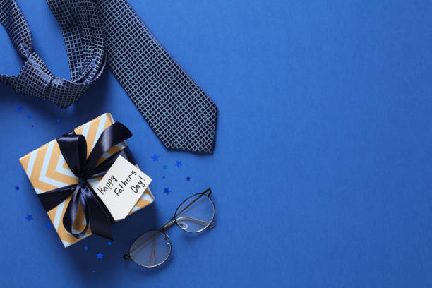 istock Happy Fathers Day flat lay composition with gift box, necktie, eyeglasses on blue table. Top view. 1389757210
