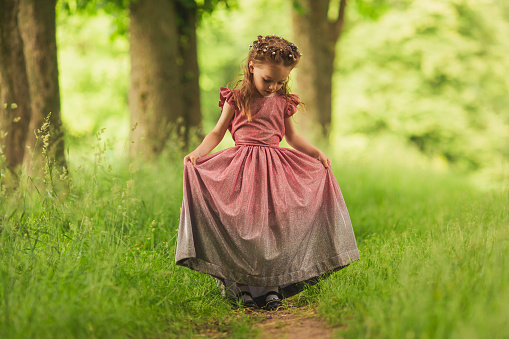 Little happy girl in a pink dress on background of spring nature. Child is playing in the meadow. Vivid emotions. Childhood concept. Rest on nature. Summer vacations. Green grass. Stylish clothes