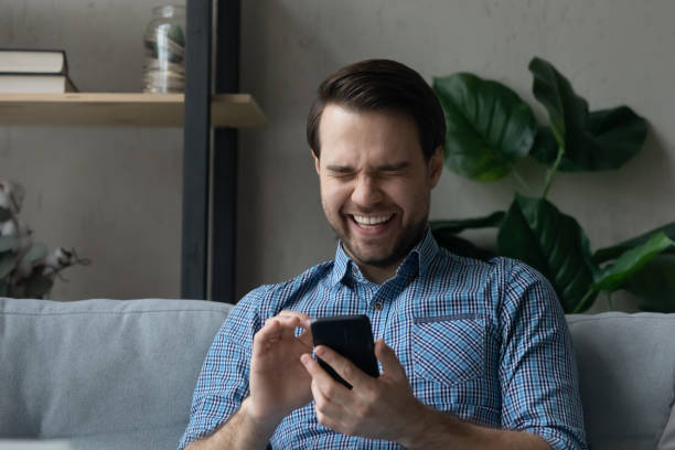 istock Man sits on sofa holds smartphone laughs on funny video 1389758503