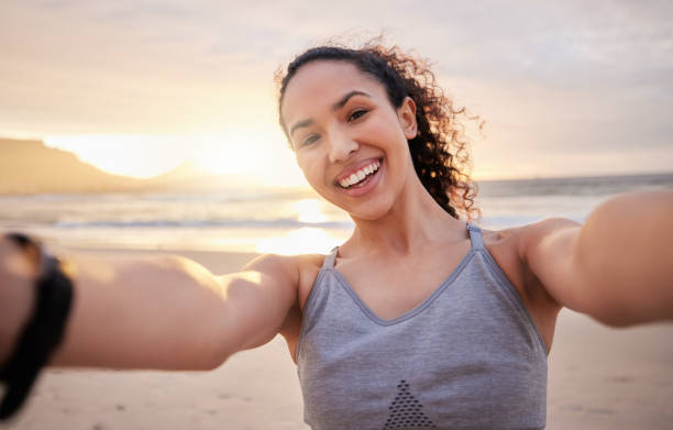 foto de uma jovem em forma tirando uma selfie na praia - real people young women women beautiful - fotografias e filmes do acervo