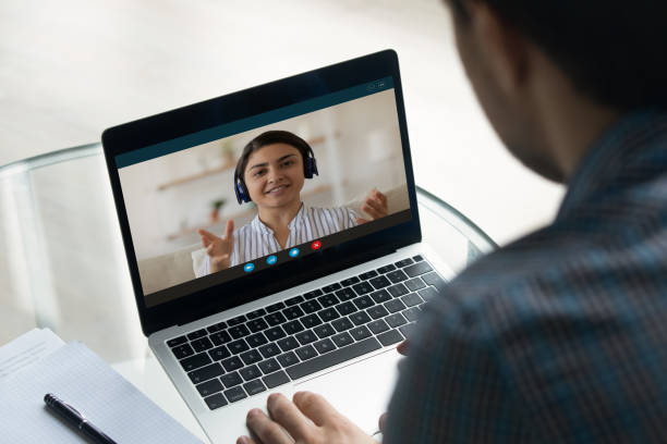 Indian woman engaged in videoconference, laptop screen over man shoulder Indian woman take part in videoconference by work or study, laptop screen view over guy shoulder. Man sit at table looks at computer listen colleague or getting online consultation, video call concept online tutors stock pictures, royalty-free photos & images