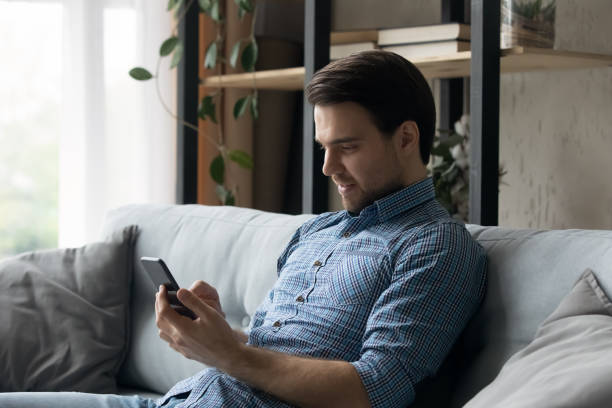 istock Young man sit on sofa with smart phone 1389760072