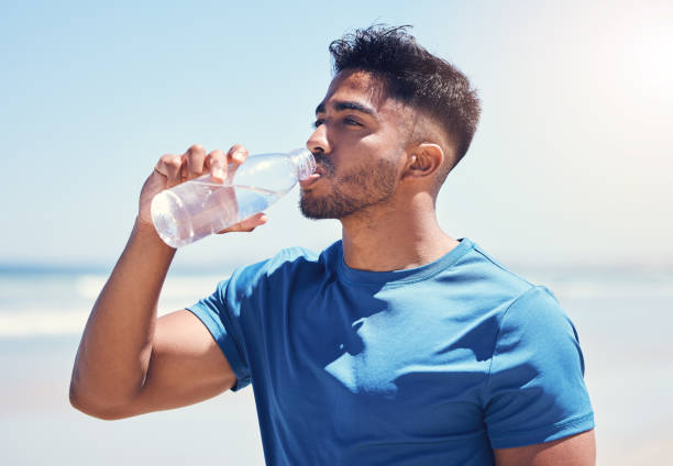 istock Shot of a man drinking water while out for a run on the beach 1389761026